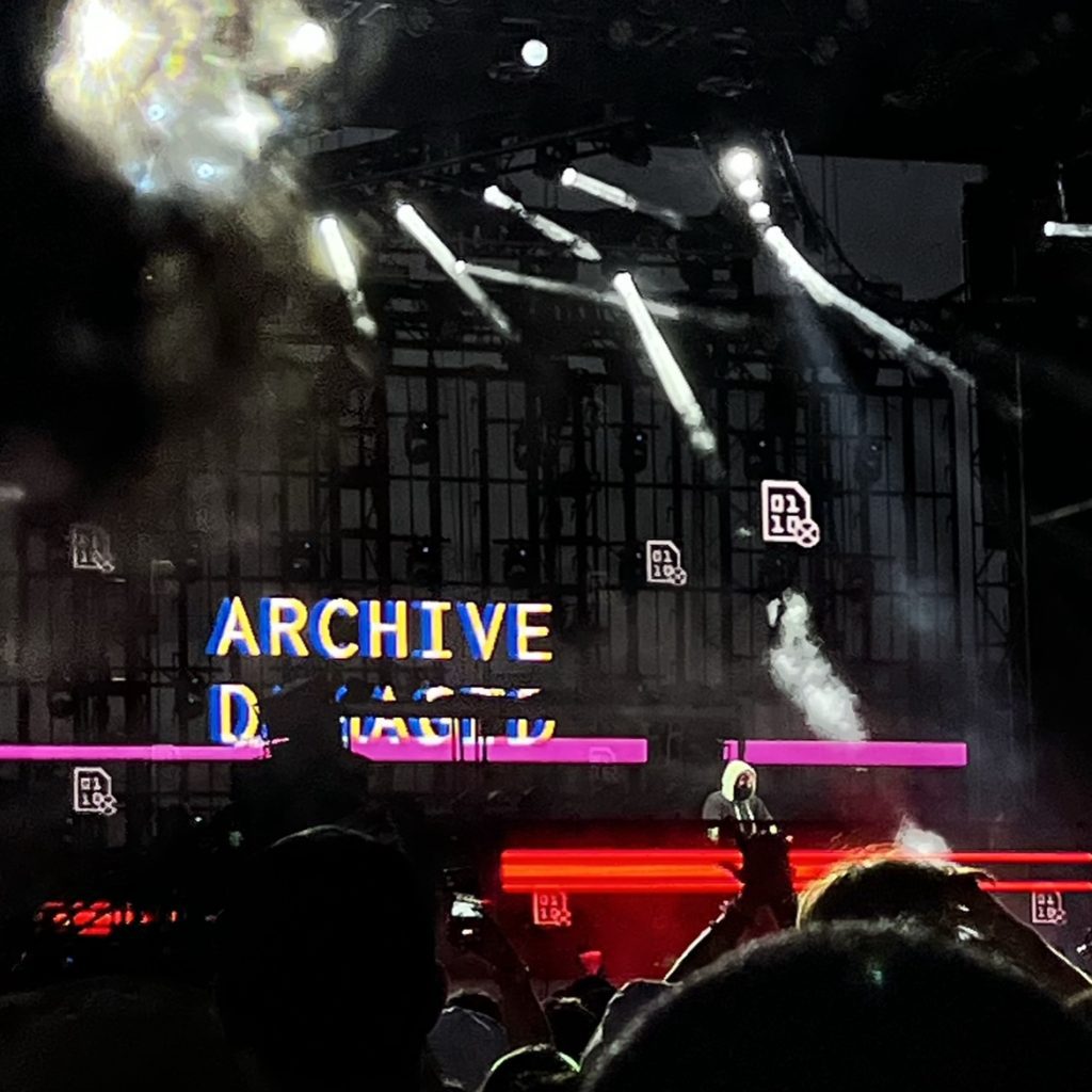 Alan Walker on stage with the top of a few heads in the foreground. His background visual says "Archive" and obscured is possibly the word "Damaged"