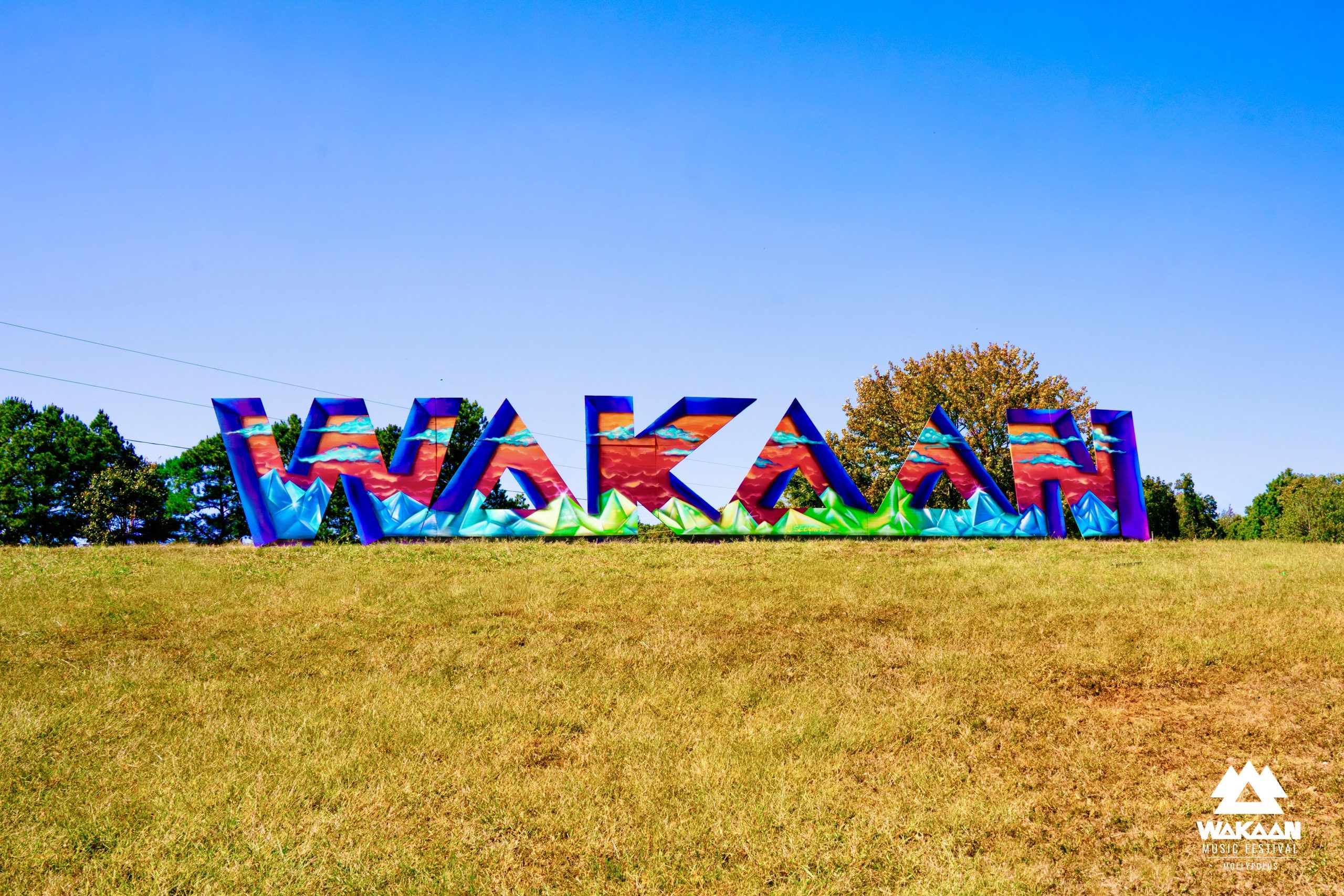 Colorful oversized letters spelling “WAKAAN” stand across a grassy hillside beneath a clear blue sky at WAKAAN Music Festival.